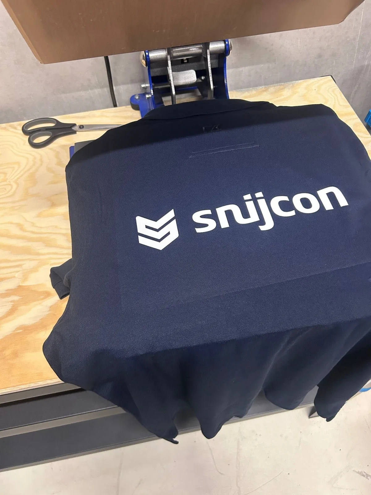 Donkerblauw shirt met bedrijfslogo onder de transferpers in het atelier