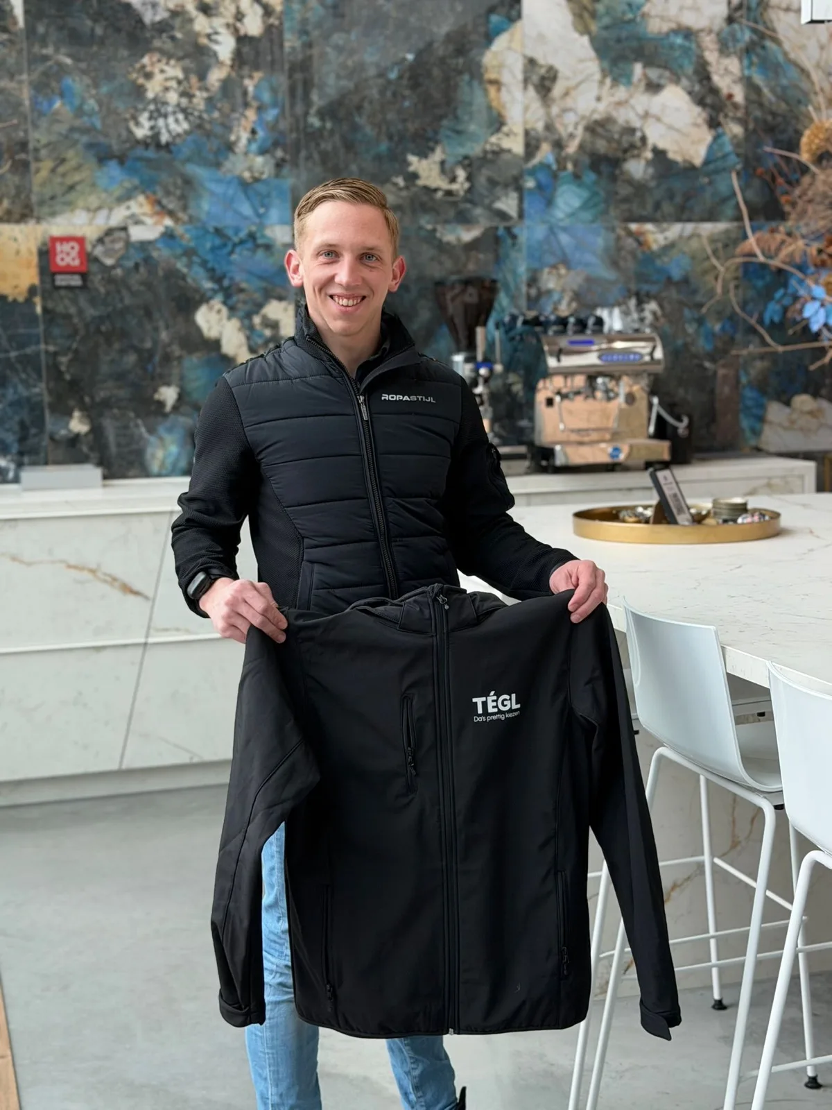 Medewerker toont een zwarte softshell jas met bedrijfslogo op de borst